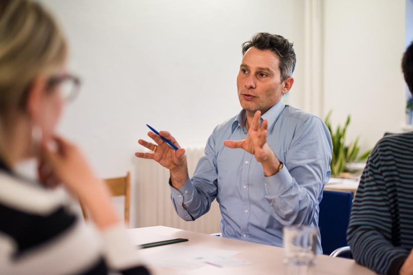 Ein Abteilungsleiter sitzt mit anderen am Tisch und erklärt mit großen Gesten