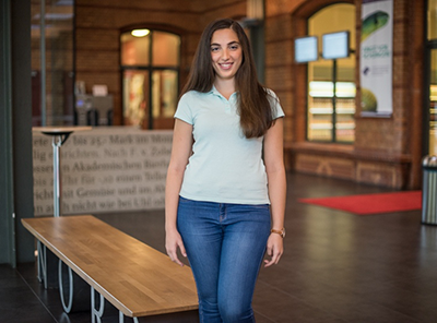 Praktikantin, steht im Foyer eines Studentenwerks und lächelt in die Kamera