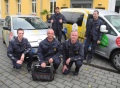 Vorschau: Das Hausmeister-/techniker-Team (5 Personen) auf dem Uni-Gelände, positioniert vor dem Umzugswagen des Studierendenwerks 